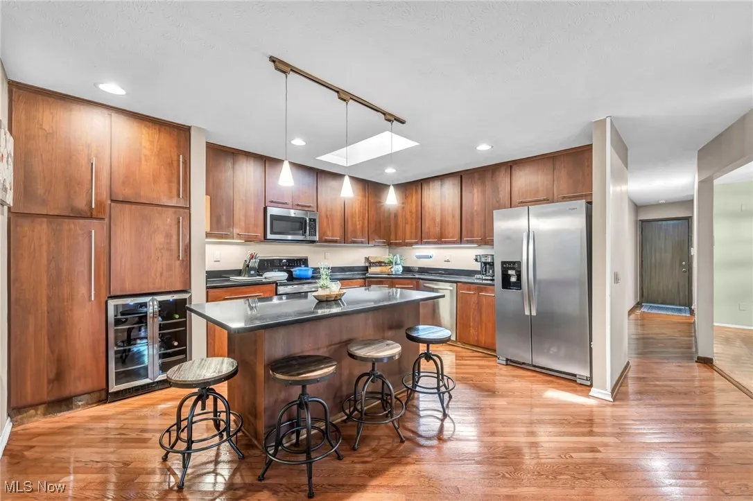 Kitchen with appliances with stainless steel finishes, hanging light fixtures, wine cooler, a skylight, and a kitchen bar