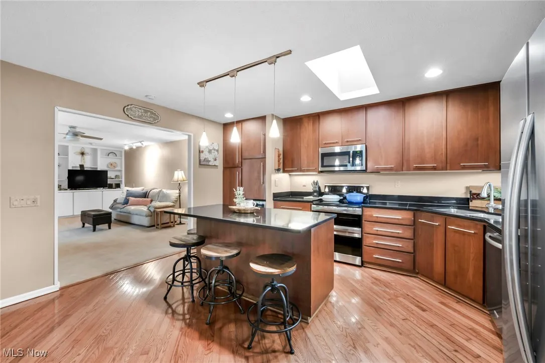 Kitchen with rail lighting, a kitchen island, stainless steel appliances, a kitchen bar, and a skylight