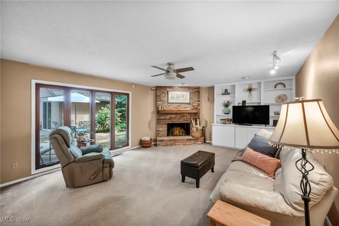 Living room featuring carpet, a brick fireplace, ceiling fan, and built in features