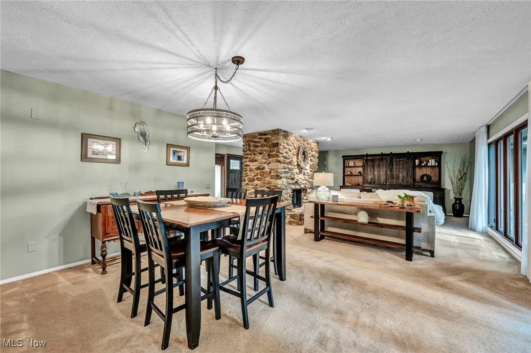Dining space with light carpet, a textured ceiling, healthy amount of natural light, a fireplace, and a chandelier