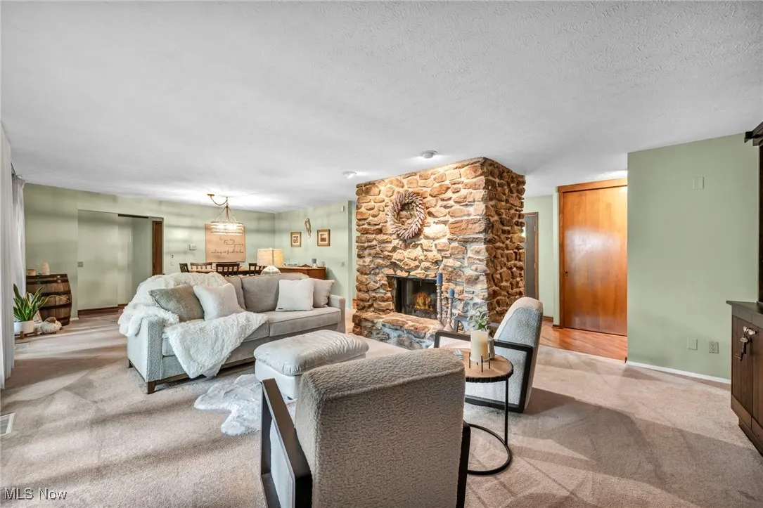 Living area with light carpet, a stone fireplace, and a textured ceiling