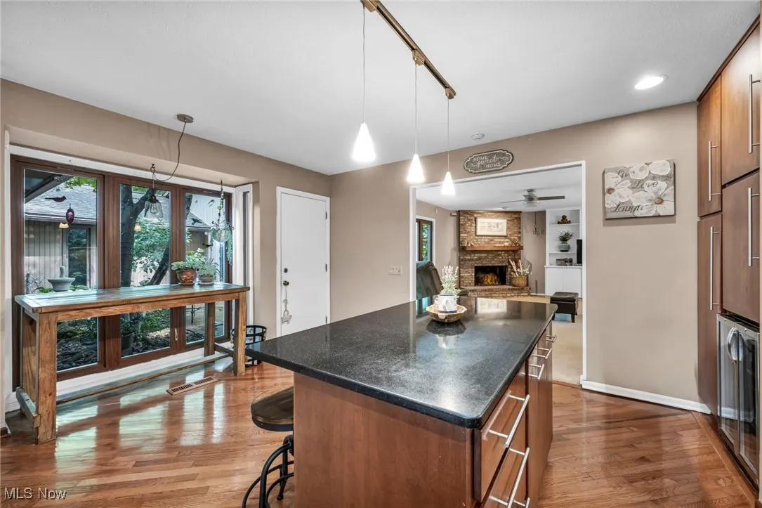 Kitchen with brown cabinets, dark wood-type flooring, hanging light fixtures, a brick fireplace, and recessed lighting