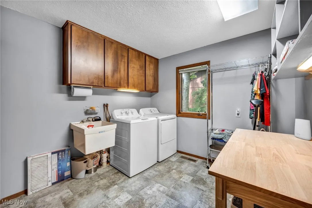 Laundry room featuring a textured ceiling, cabinet space, washing machine and clothes dryer, and stone finish flooring