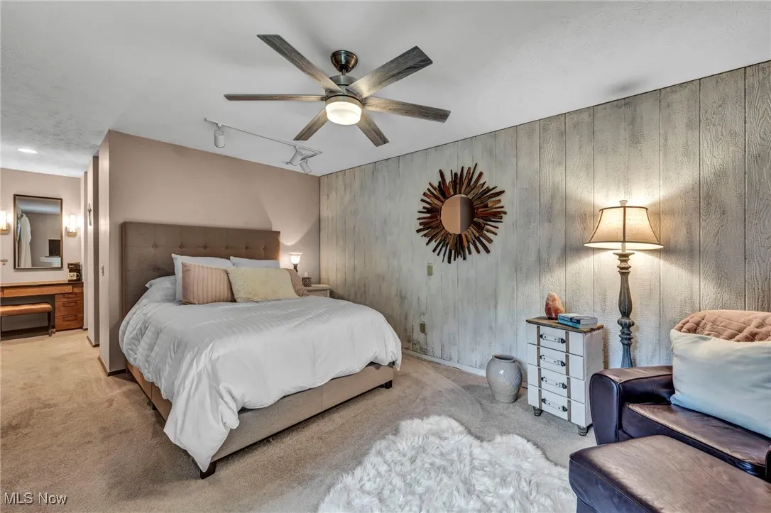 Bedroom with carpet floors, wooden walls, track lighting, and ceiling fan