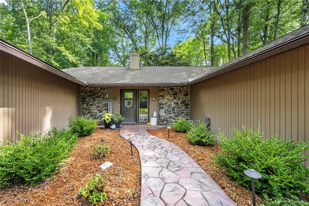 Doorway to property with stone siding, a chimney, a shingled roof, and an attached garage