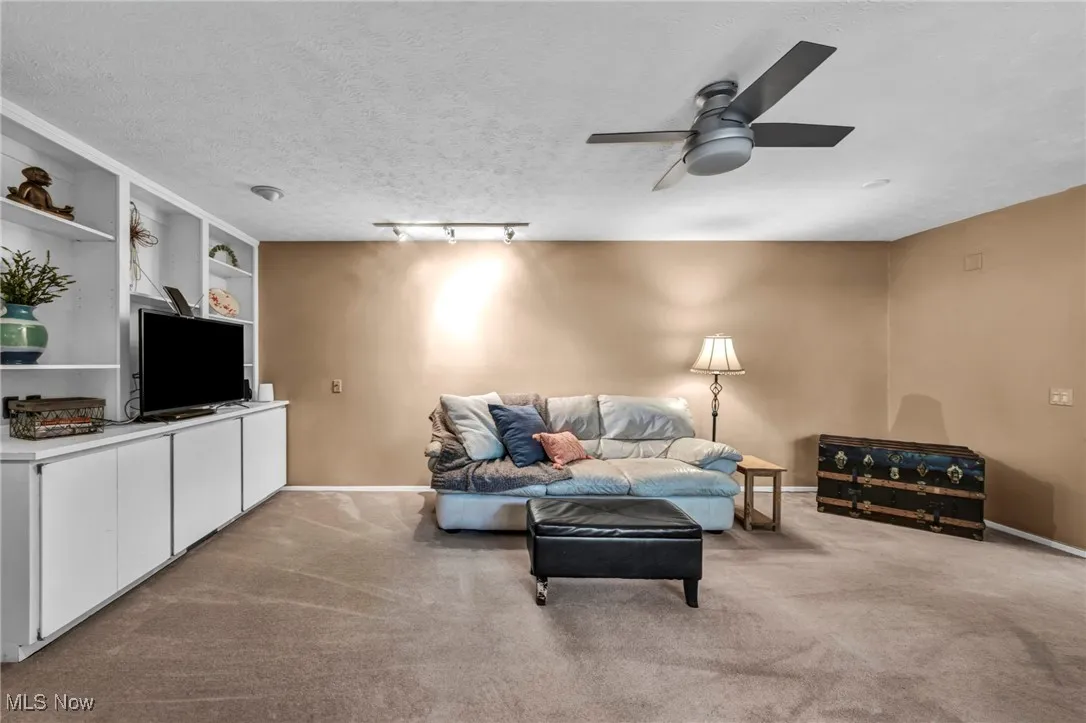 Living area with carpet, built in shelves, a ceiling fan, and a textured ceiling