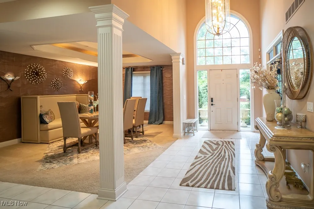 Tiled entrance foyer with carpet, ornate columns, healthy amount of natural light, and a high ceiling