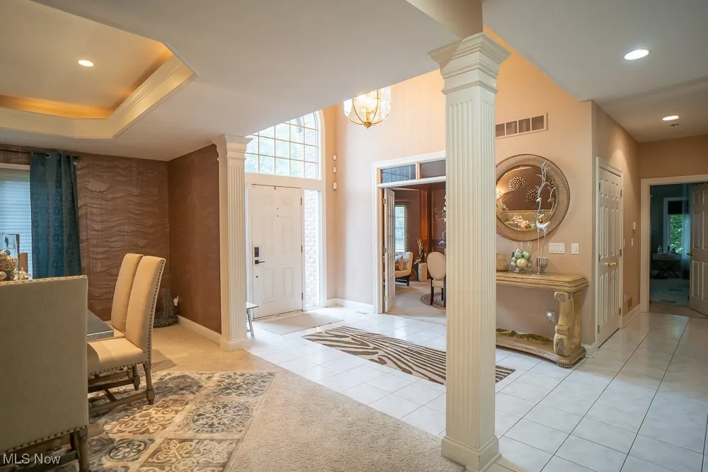 Foyer entrance featuring recessed lighting, light tile patterned floors, a chandelier, a tray ceiling, and decorative columns