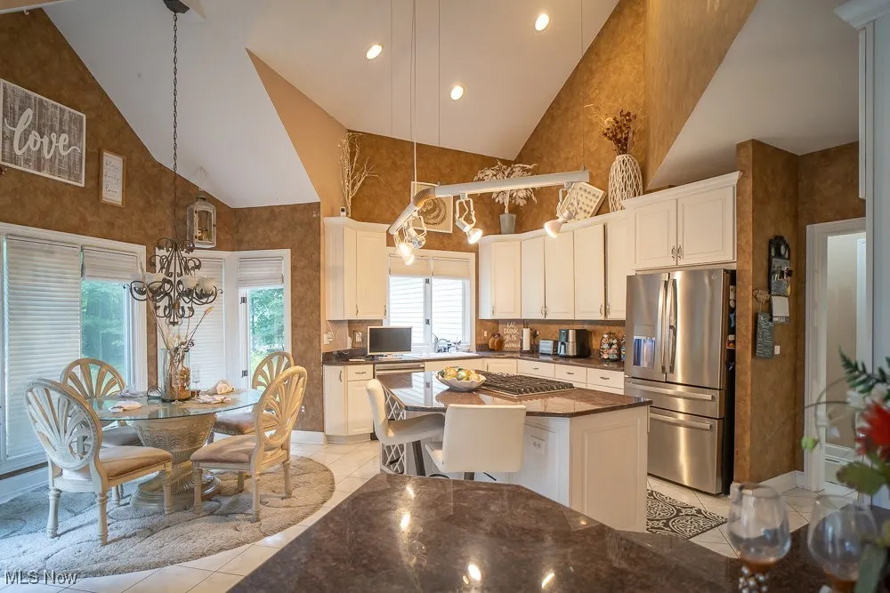 Kitchen with high vaulted ceiling, a chandelier, stainless steel refrigerator with ice dispenser, recessed lighting, and dark stone countertops