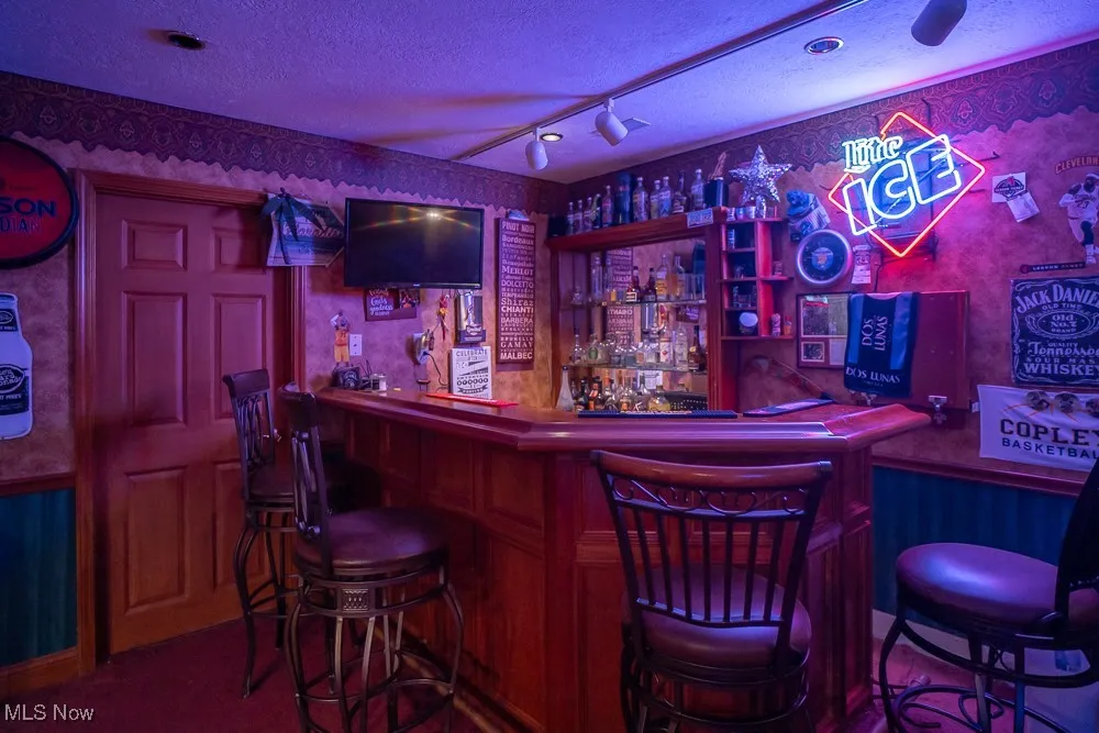 Indoor dry bar featuring track lighting, wallpapered walls, a textured ceiling, and wainscoting