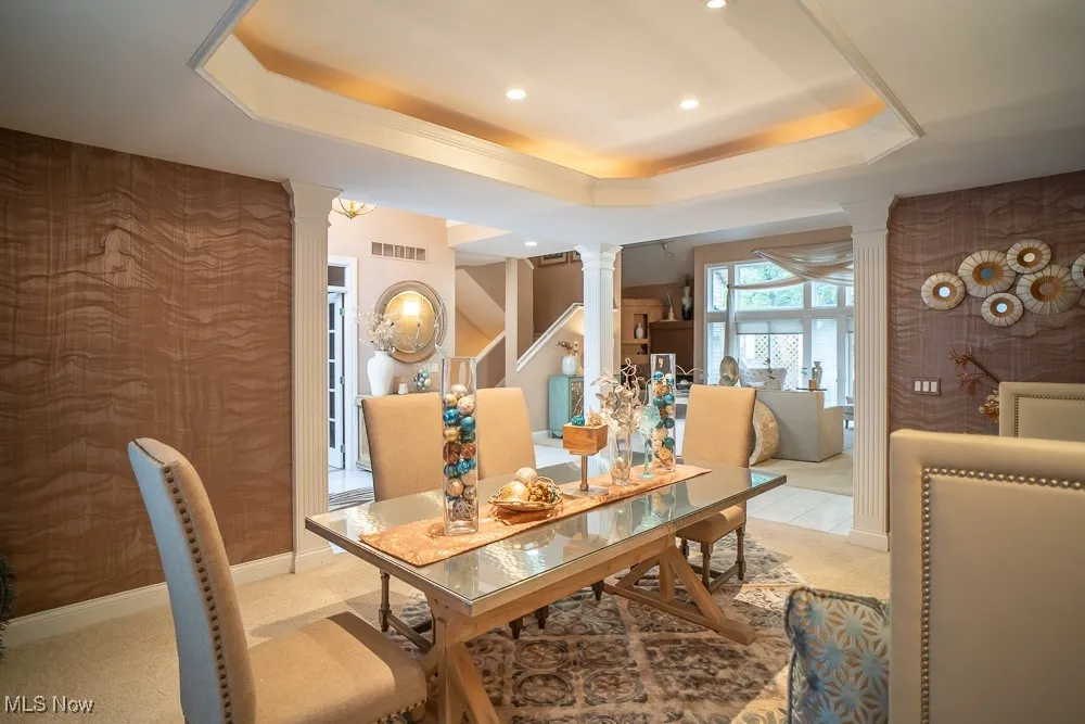 Dining space featuring ornate columns, a tray ceiling, stairs, recessed lighting, and light colored carpet