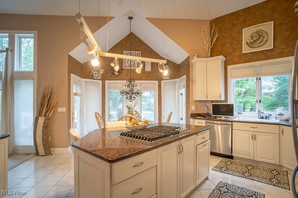 Kitchen featuring dark stone counters, stainless steel appliances, decorative light fixtures, light tile patterned floors, and a kitchen island