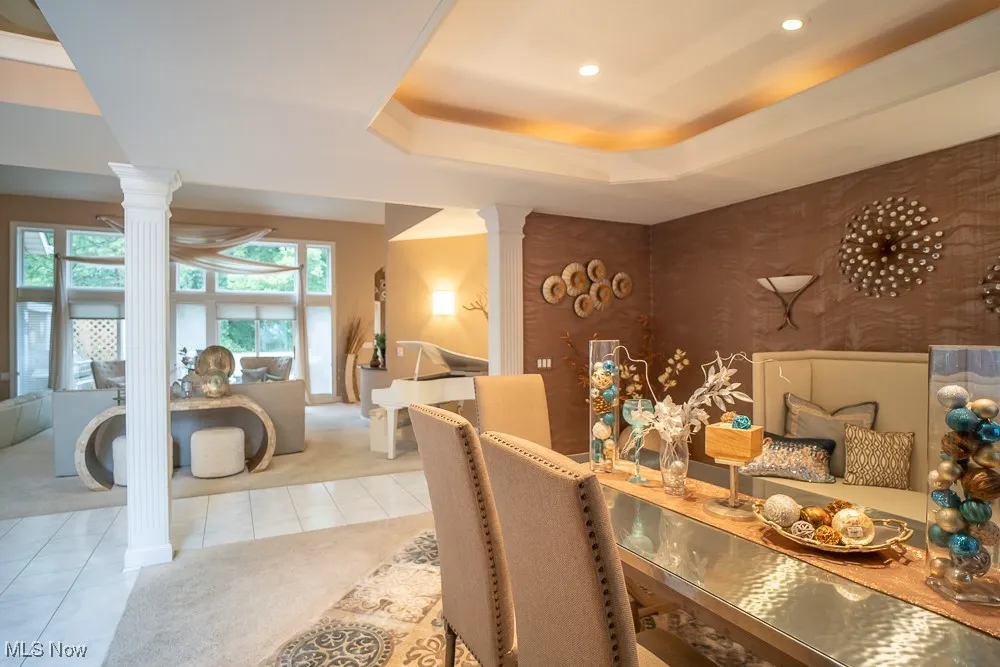 Carpeted dining area featuring a raised ceiling, decorative columns, and tile patterned flooring