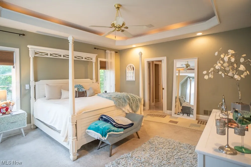 Bedroom with a raised ceiling, carpet, and ceiling fan