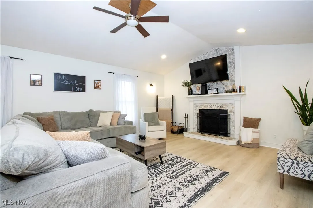 Living area featuring lofted ceiling, light wood-style flooring, a stone fireplace, ceiling fan, and recessed lighting