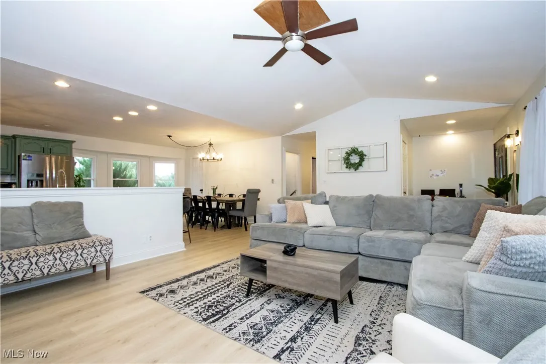 Living room with vaulted ceiling, recessed lighting, light wood-style floors, ceiling fan, and a chandelier