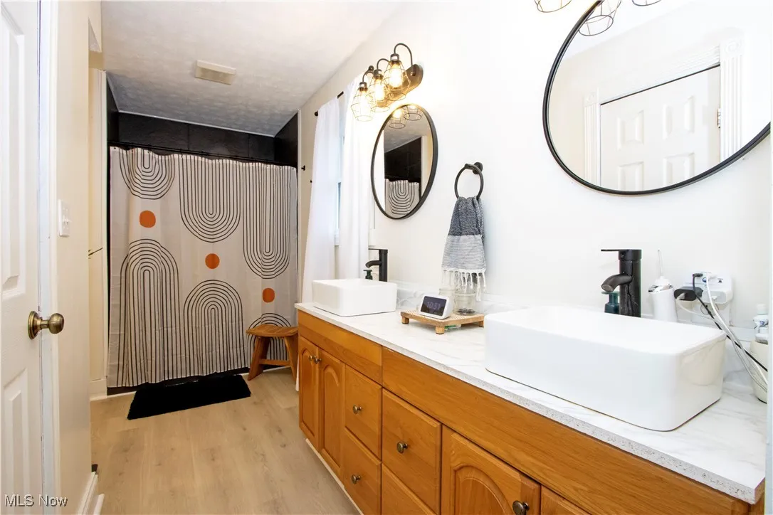Full bath featuring light wood-style flooring, double vanity, and a shower with shower curtain