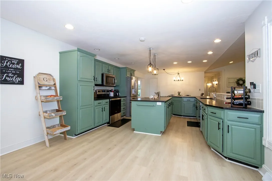 Kitchen with green cabinets, appliances with stainless steel finishes, a kitchen island, light wood-type flooring, and recessed lighting
