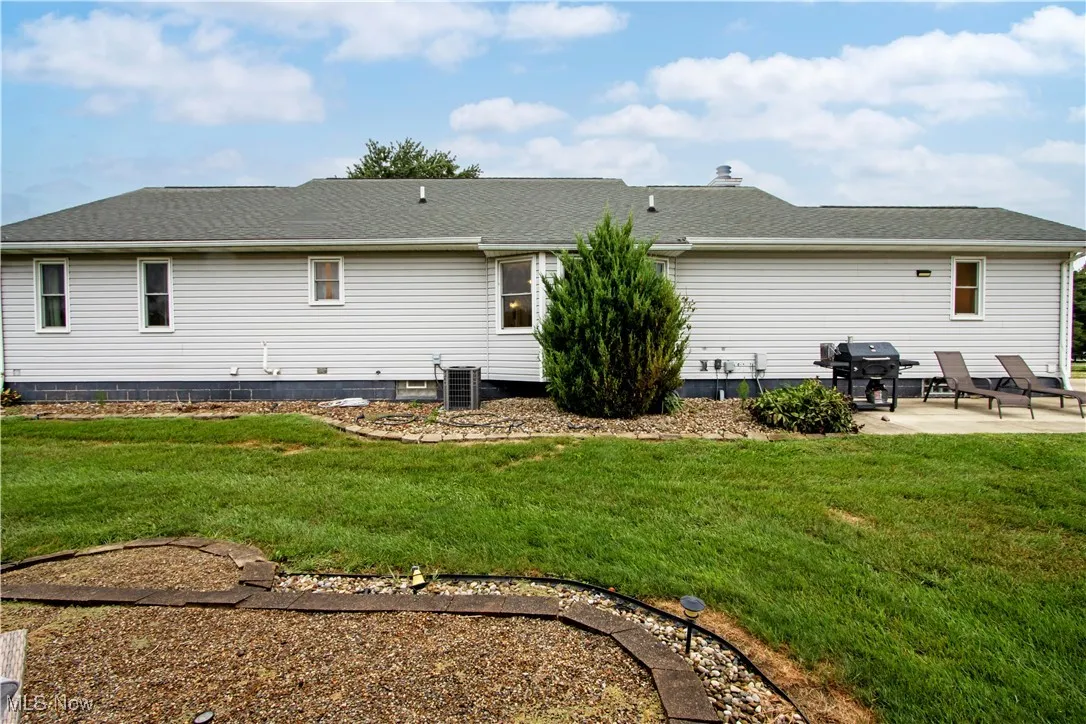 Back of house featuring a shingled roof, a lawn, and a patio