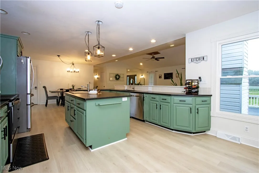 Kitchen featuring green cabinetry, light wood finished floors, a kitchen island, hanging light fixtures, and recessed lighting