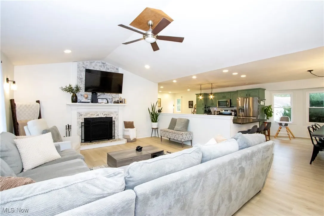 Living area with lofted ceiling, light wood-style flooring, a fireplace, recessed lighting, and a ceiling fan