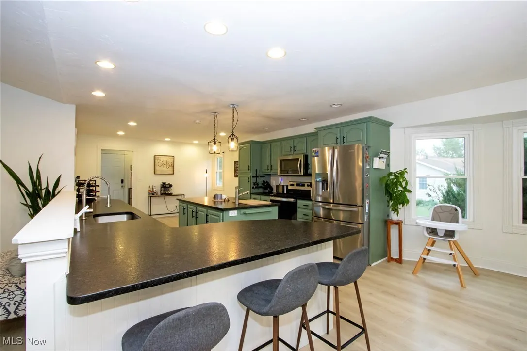 Kitchen with green cabinetry, a breakfast bar area, a kitchen island, appliances with stainless steel finishes, and light wood finished floors