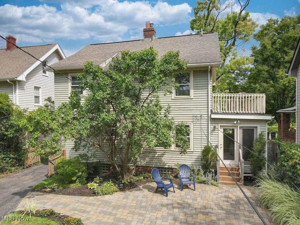 Back exterior of home with lilac tree, paver patio and second floor balcony.