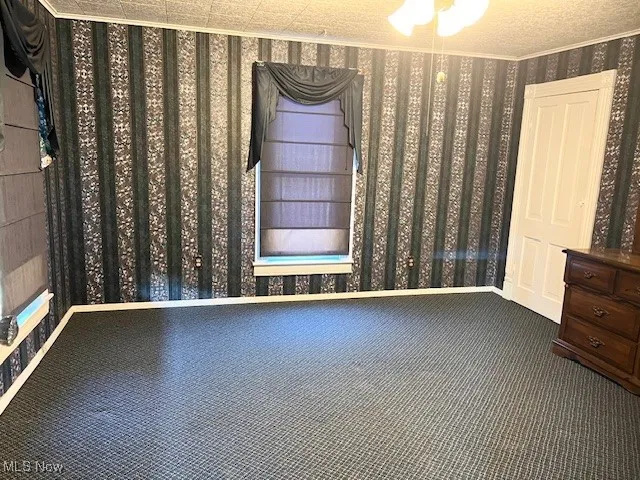 Unfurnished room with dark colored carpet, wallpapered walls, and crown molding