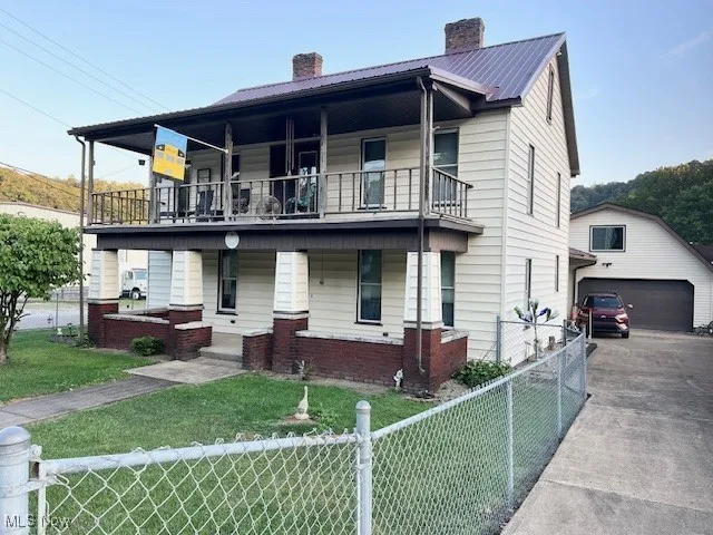 View of front of property with a chimney, a metal roof, covered porch, a fenced front yard, and brick siding