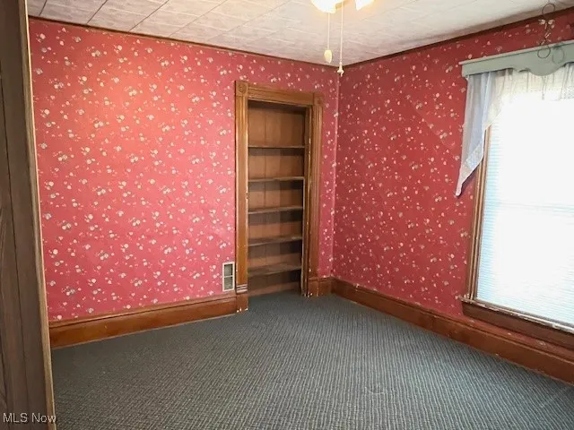 Spare room with wallpapered walls and dark colored carpet