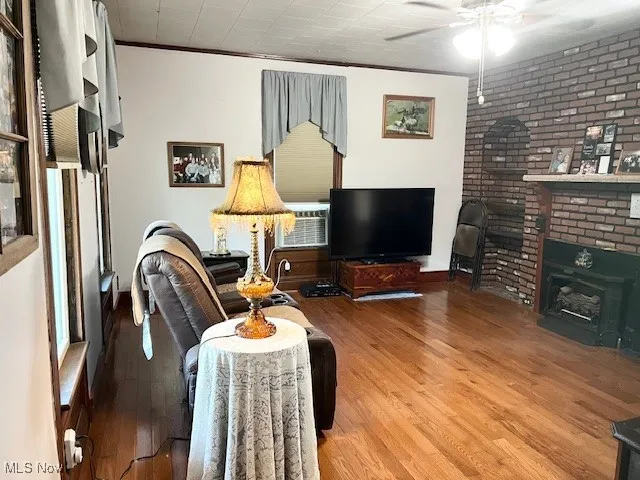 Living room with ornamental molding, a ceiling fan, wood finished floors, brick wall, and a wood stove