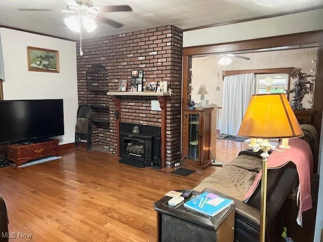 Living room featuring a ceiling fan, ornamental molding, wood finished floors, and a wood stove
