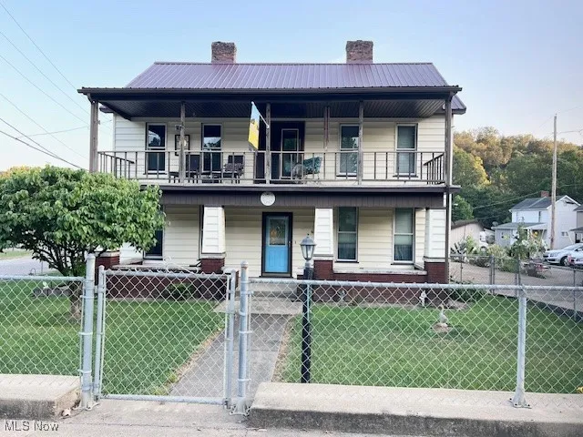 View of front facade featuring a gate, a chimney, a metal roof, and covered porch
