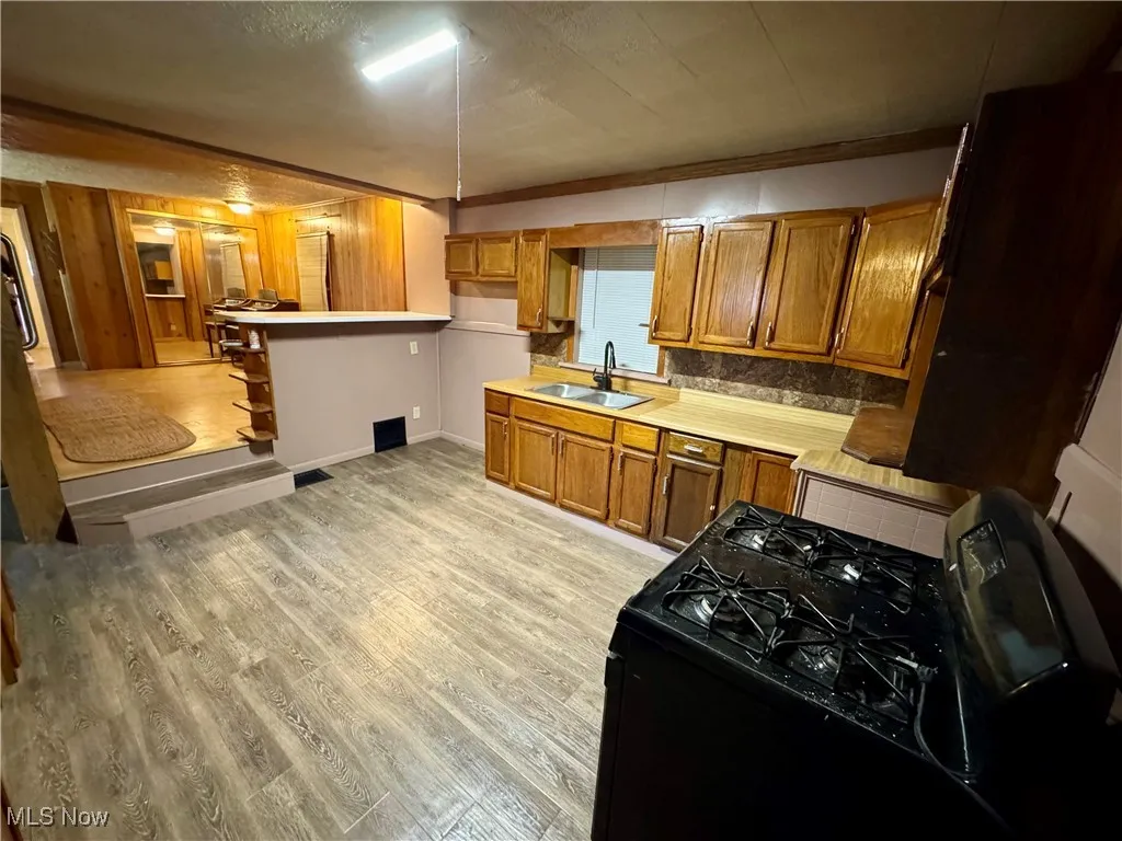 Kitchen featuring brown cabinets, black range with gas cooktop, light countertops, light wood-type flooring, and decorative backsplash