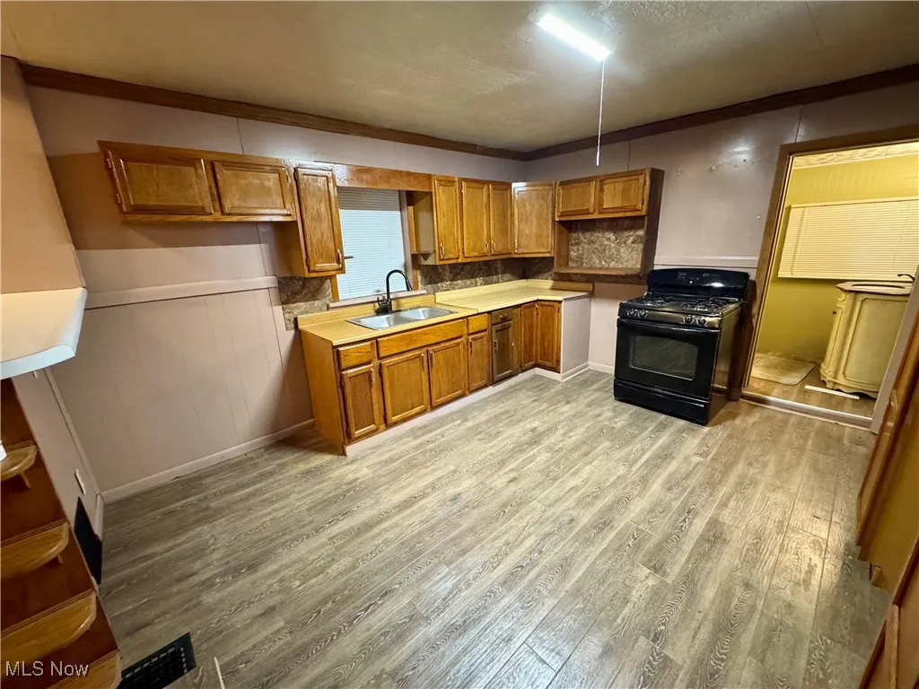 Kitchen featuring brown cabinets, ornamental molding, light countertops, black gas range, and light wood finished floors