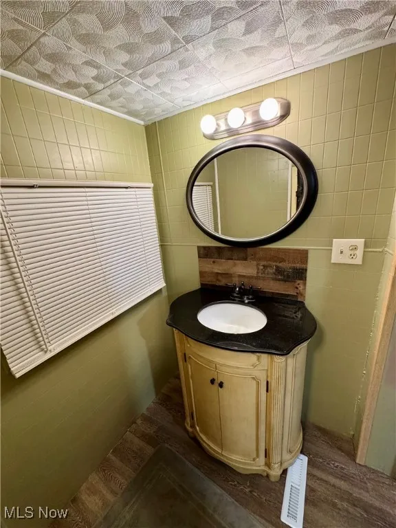 Bathroom with vanity, tile walls, and dark wood-style flooring