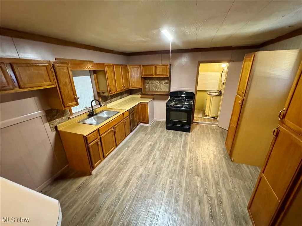 Kitchen featuring brown cabinets, light wood-type flooring, gas stove, light countertops, and crown molding