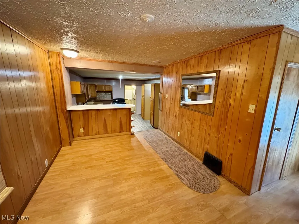 Hall featuring wooden walls, light wood-style flooring, and a textured ceiling