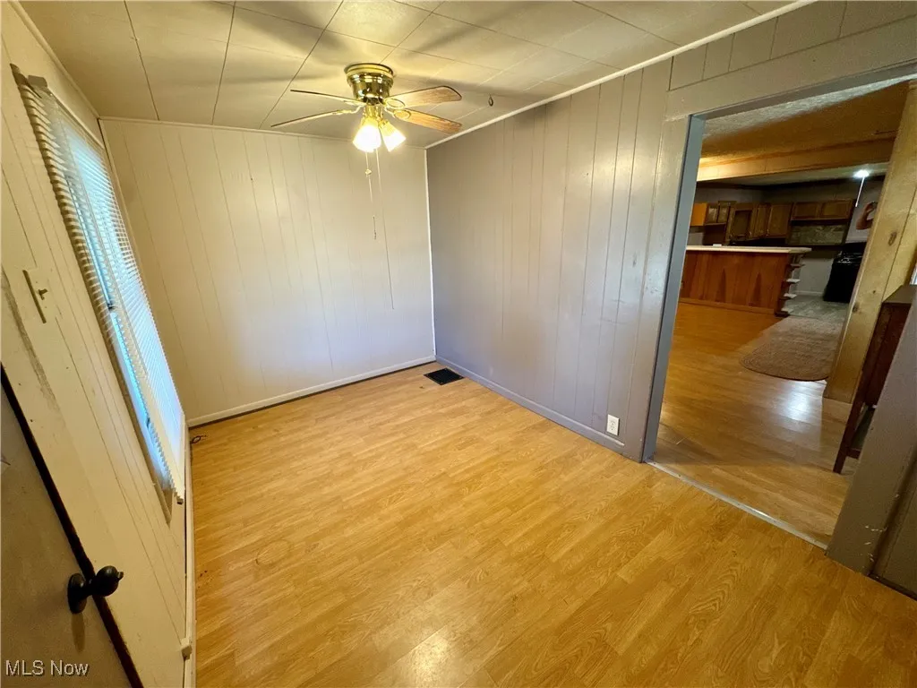 Unfurnished bedroom featuring wood walls, light wood-type flooring, and a ceiling fan