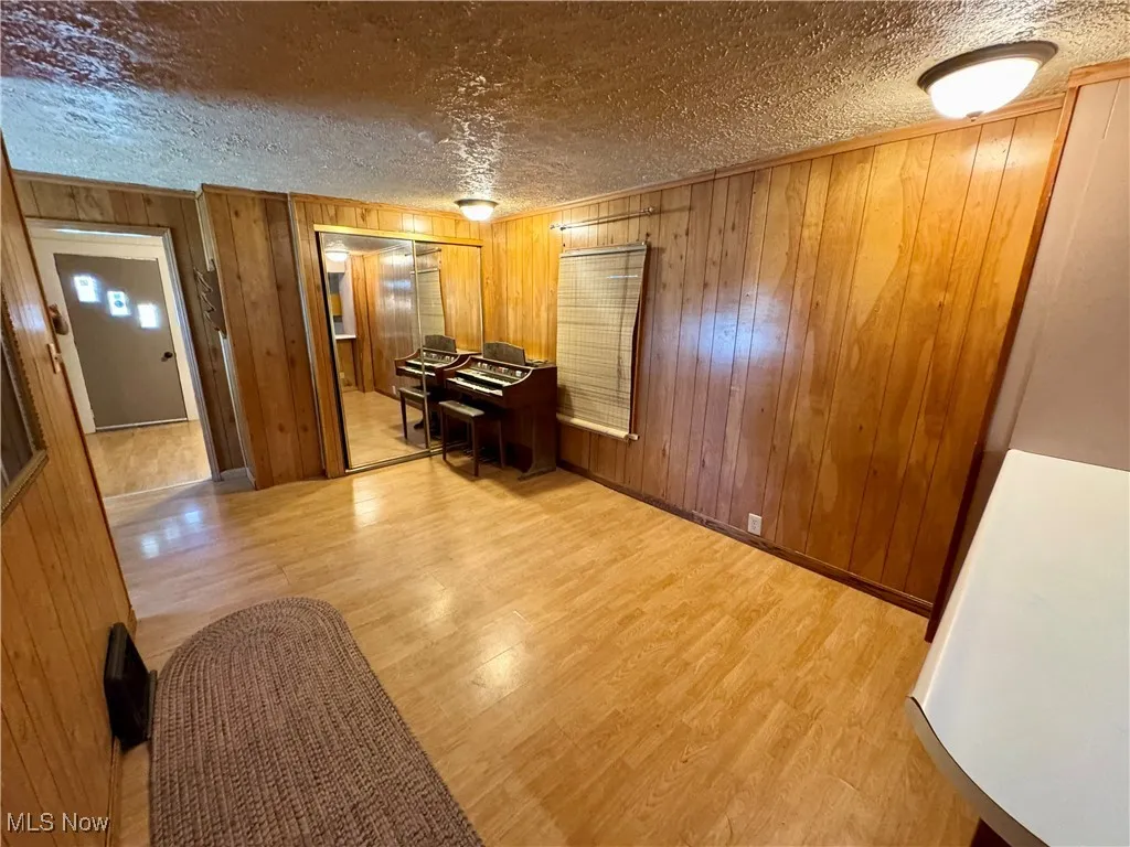 Living area featuring a textured ceiling, wood walls, and light wood-type flooring