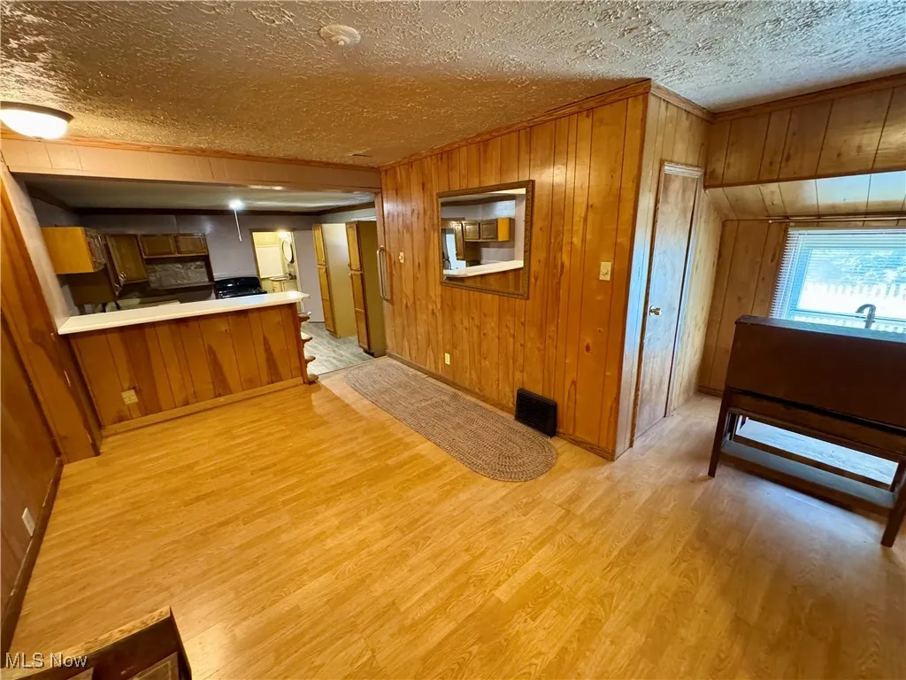 Kitchen with a peninsula, brown cabinetry, wooden walls, light wood-type flooring, and ornamental molding