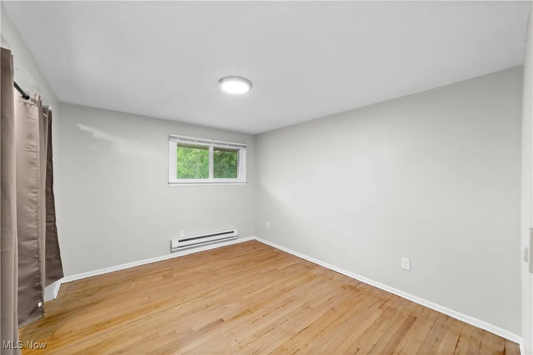 Unfurnished bedroom with light wood-type flooring, a baseboard radiator, and a barn door