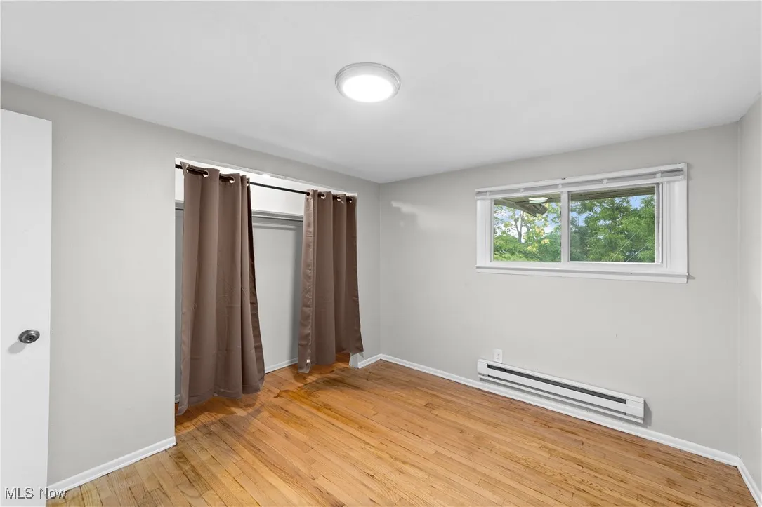 Unfurnished bedroom with light wood-style floors and baseboard heating