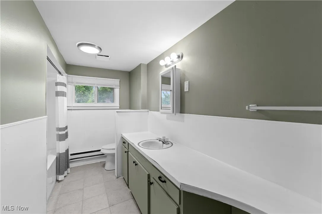 Full bathroom with vanity, shower / tub combo, a baseboard heating unit, and light tile patterned floors