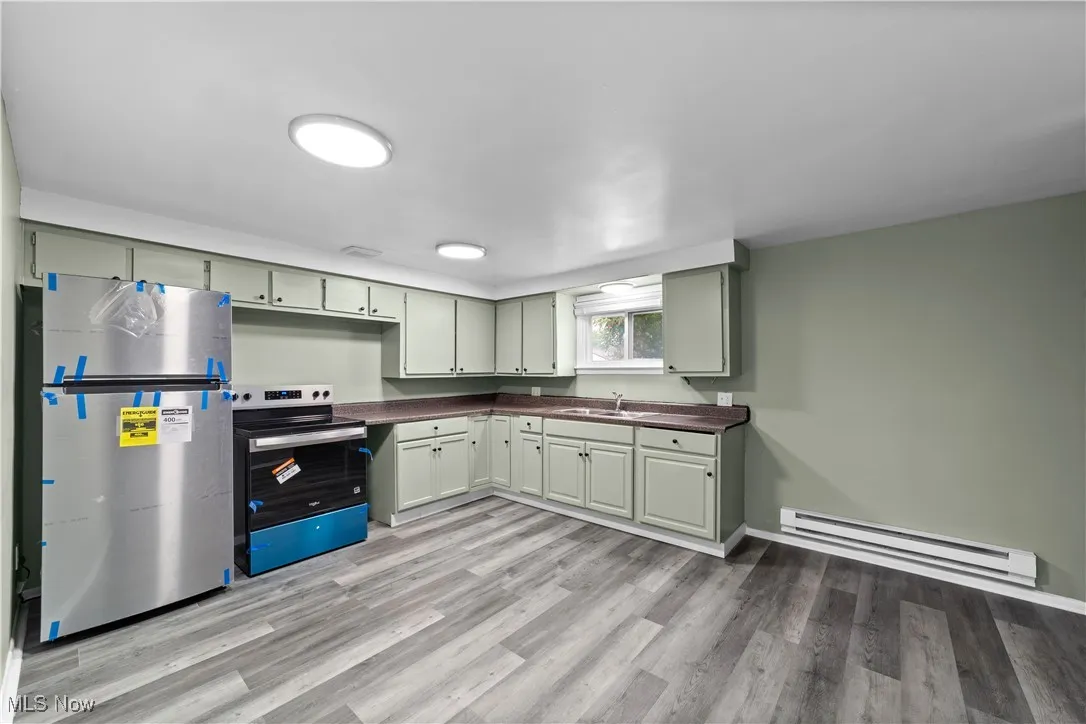 Kitchen featuring dark countertops, a baseboard heating unit, stainless steel appliances, and light wood-style flooring