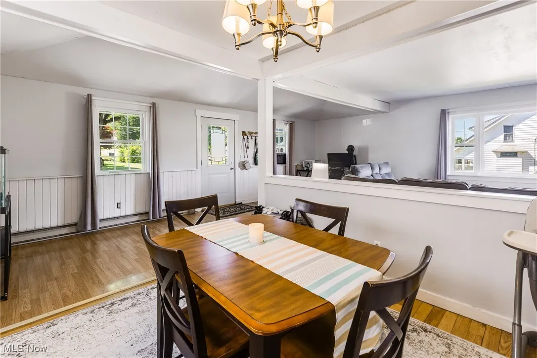 Dining area with beamed ceiling, light wood-type flooring, a chandelier, and a wainscoted wall