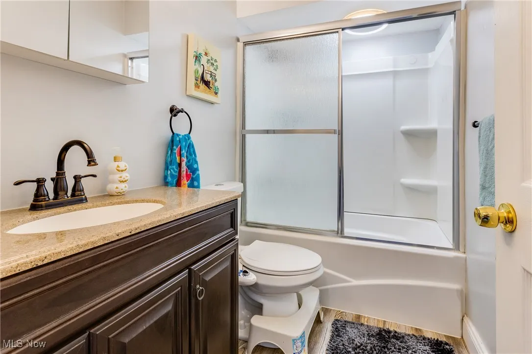 Full bathroom with enclosed tub / shower combo, vanity, and wood finished floors