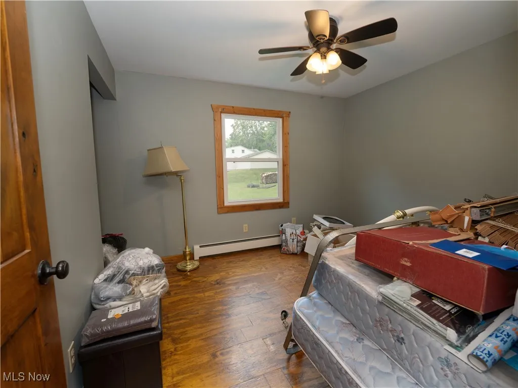 Bedroom featuring dark wood-type flooring, a baseboard radiator, and a ceiling fan