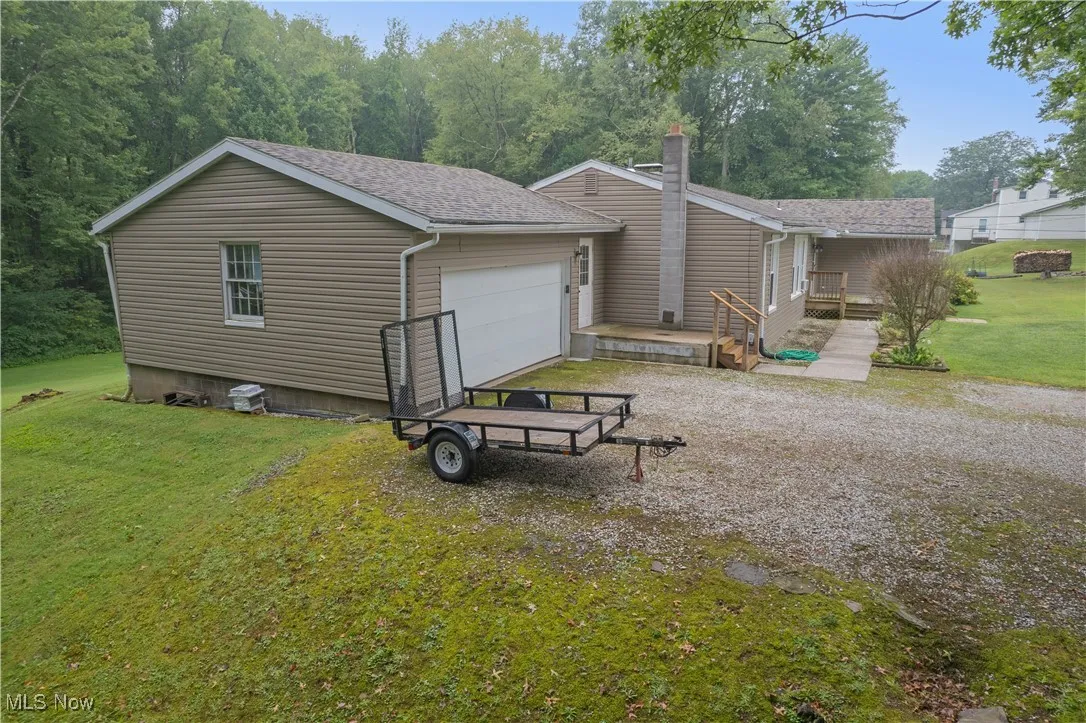 Rear view of house with a lawn, a garage, gravel driveway, roof with shingles, and a chimney