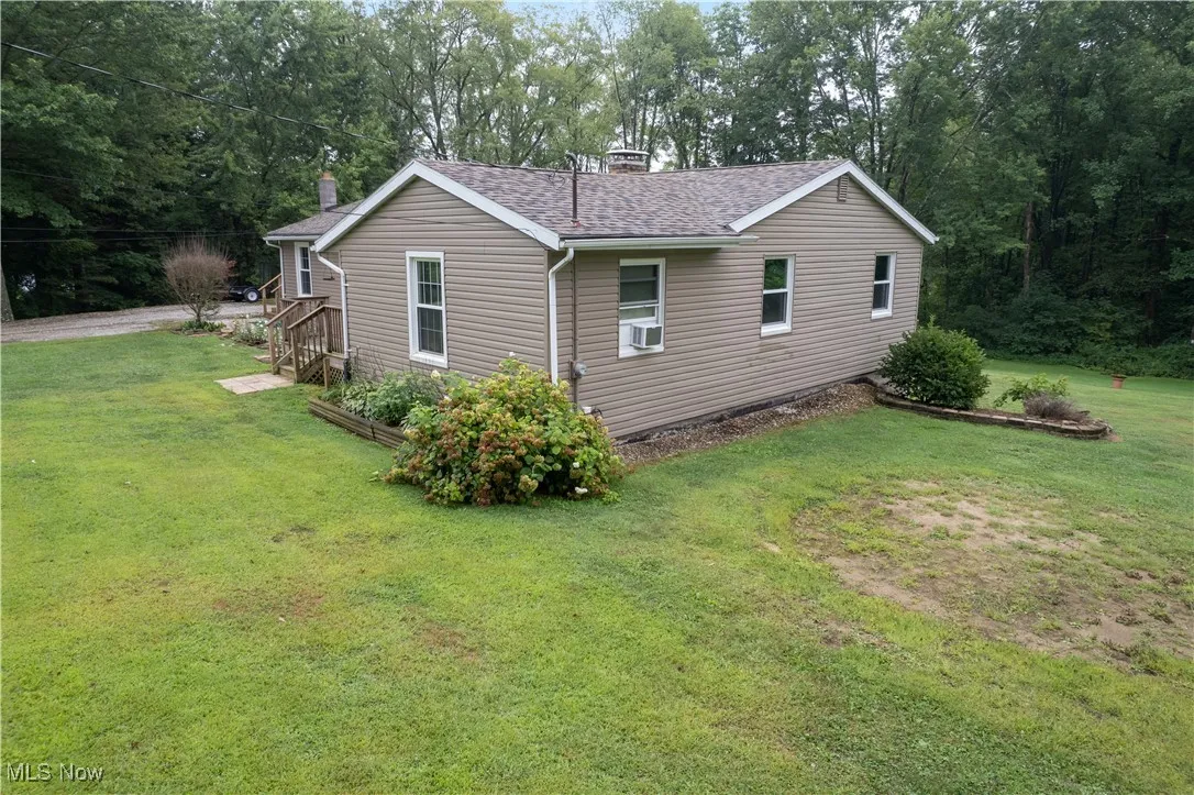 View of home's exterior with a lawn, view of scattered trees, a shingled roof, and a chimney